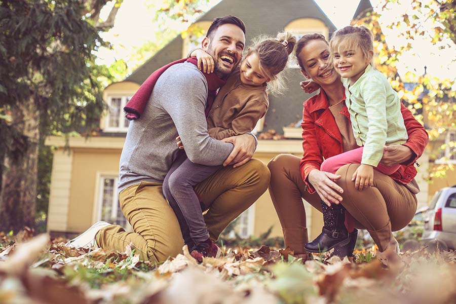 Personal Insurance - Portrait of Happy Family with Kids Playing with the Leaves Outside Their Home